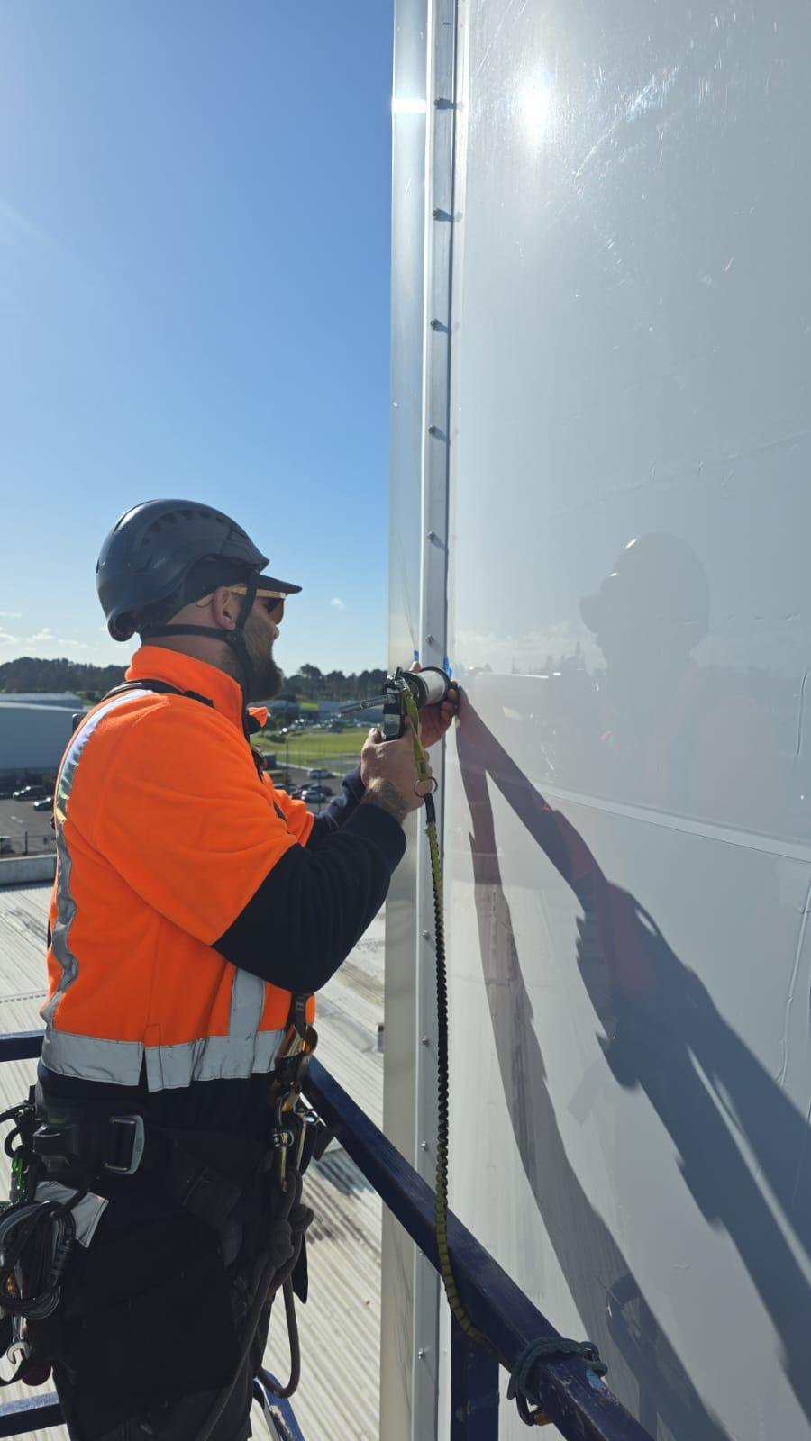 Technician applying sealant on an airport hangar facade